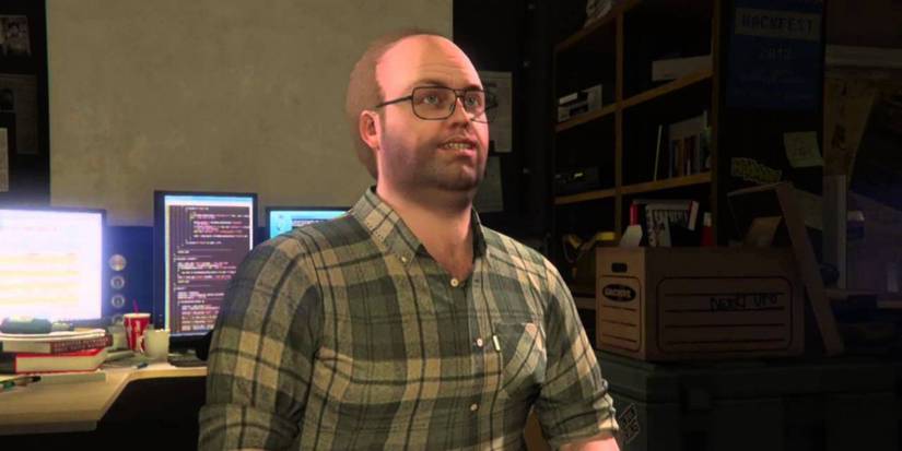 Grand Theft Auto 5 screenshot of Lester Crest smiling up from his computer desk.