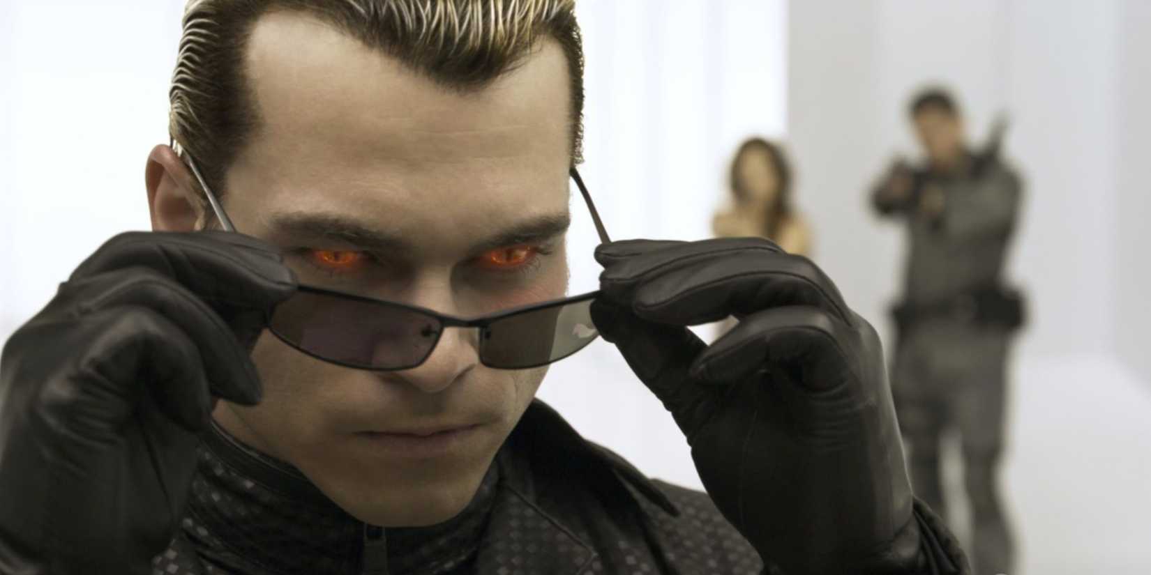 Close-up of Albert Wesker removing his sunglasses in a white room in Resident Evil: Afterlife Albert Wesker, as Claire and Chris Redfield are visible in the background.