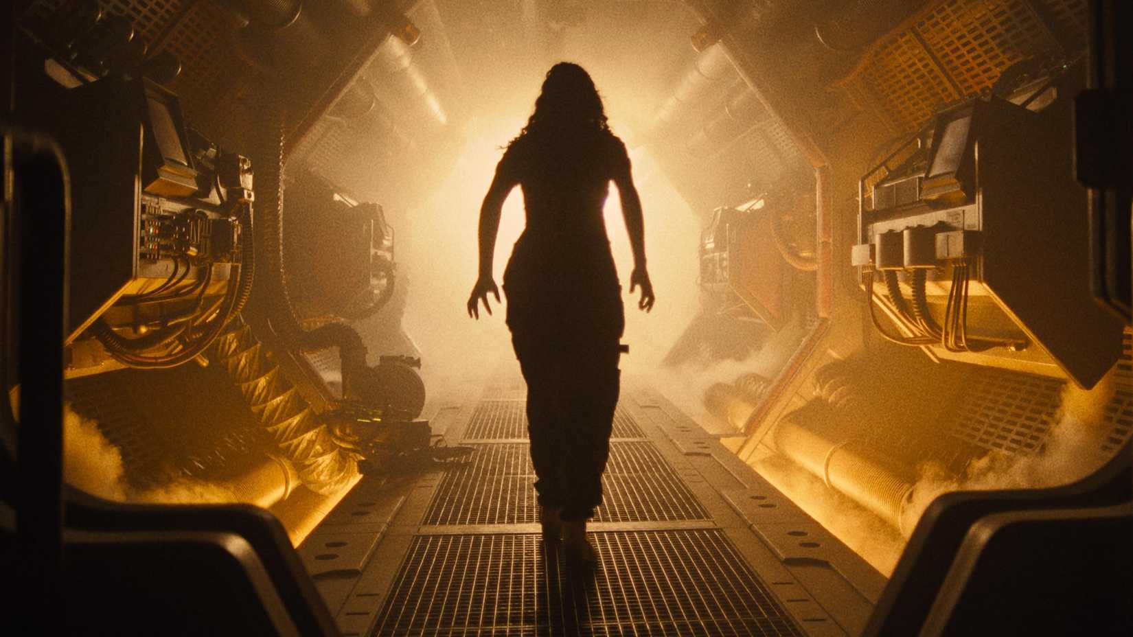 An alien Romulus woman walks down an orange corridor in a spaceship