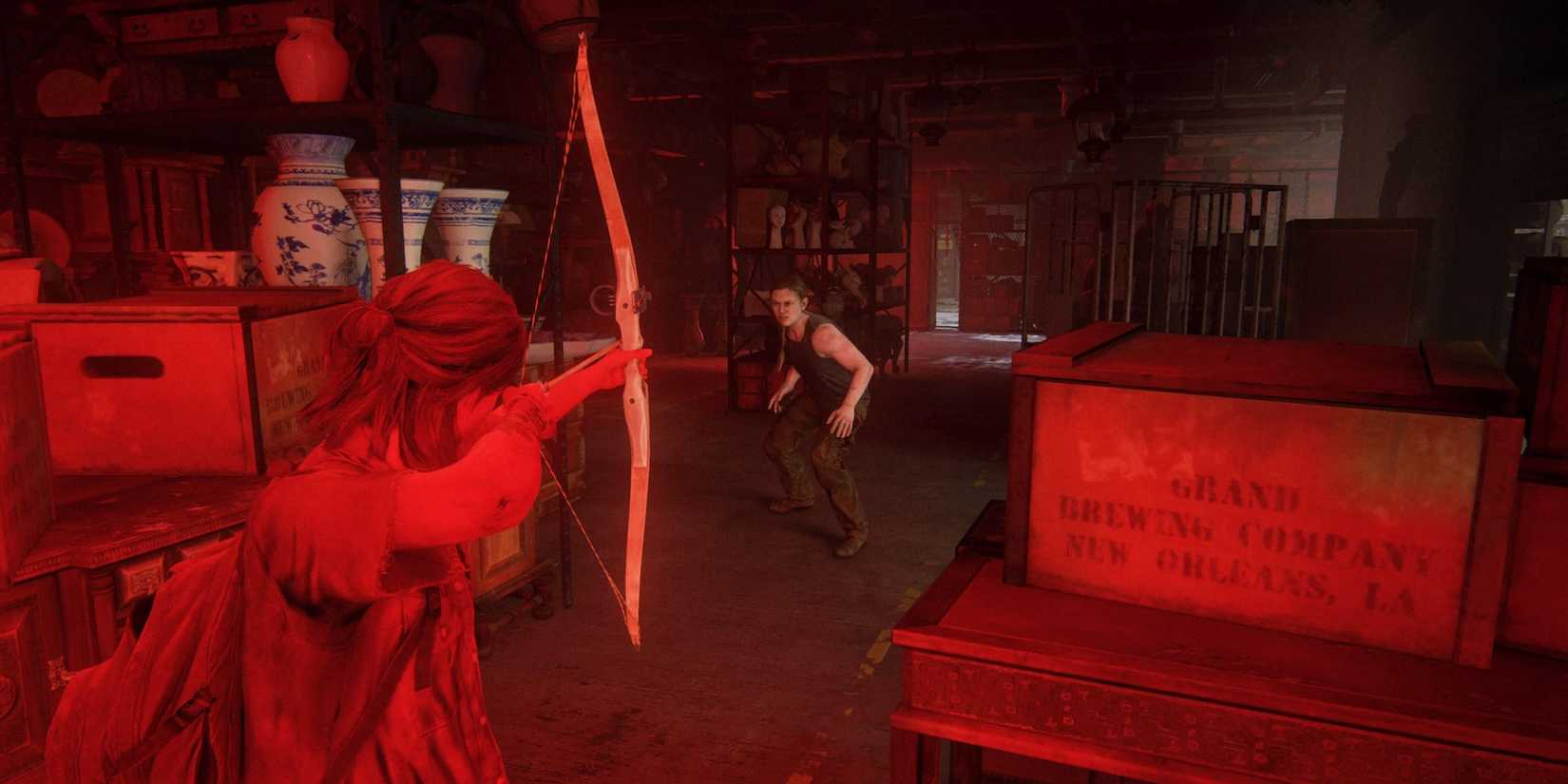 Ellie aims her bow at Abby in the glowing red light of the theater in The Last of Us Part II