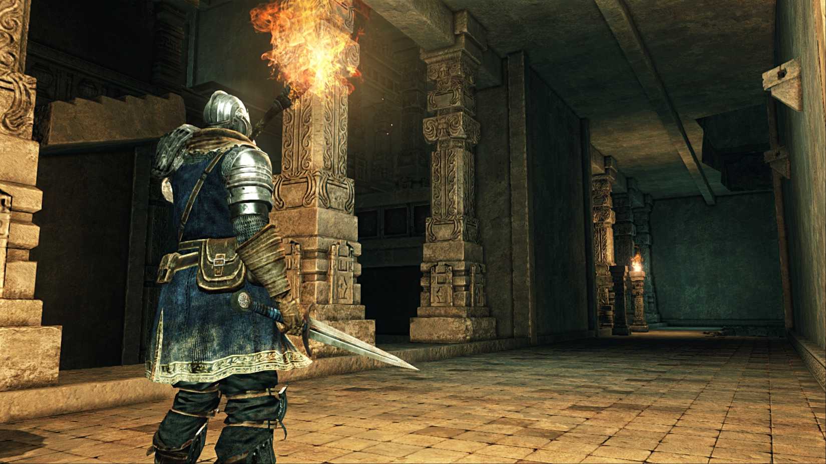 A bearer of curses walking through dimly lit and narrow hallways with a torch to light the way in Dark Souls 2.