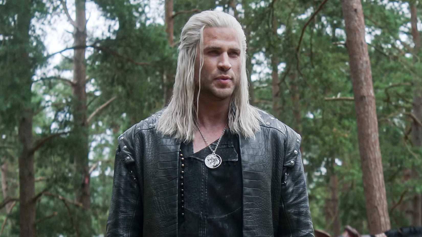 Liam Hemsworth as Geralt in The Witcher TV series, standing in a forest.