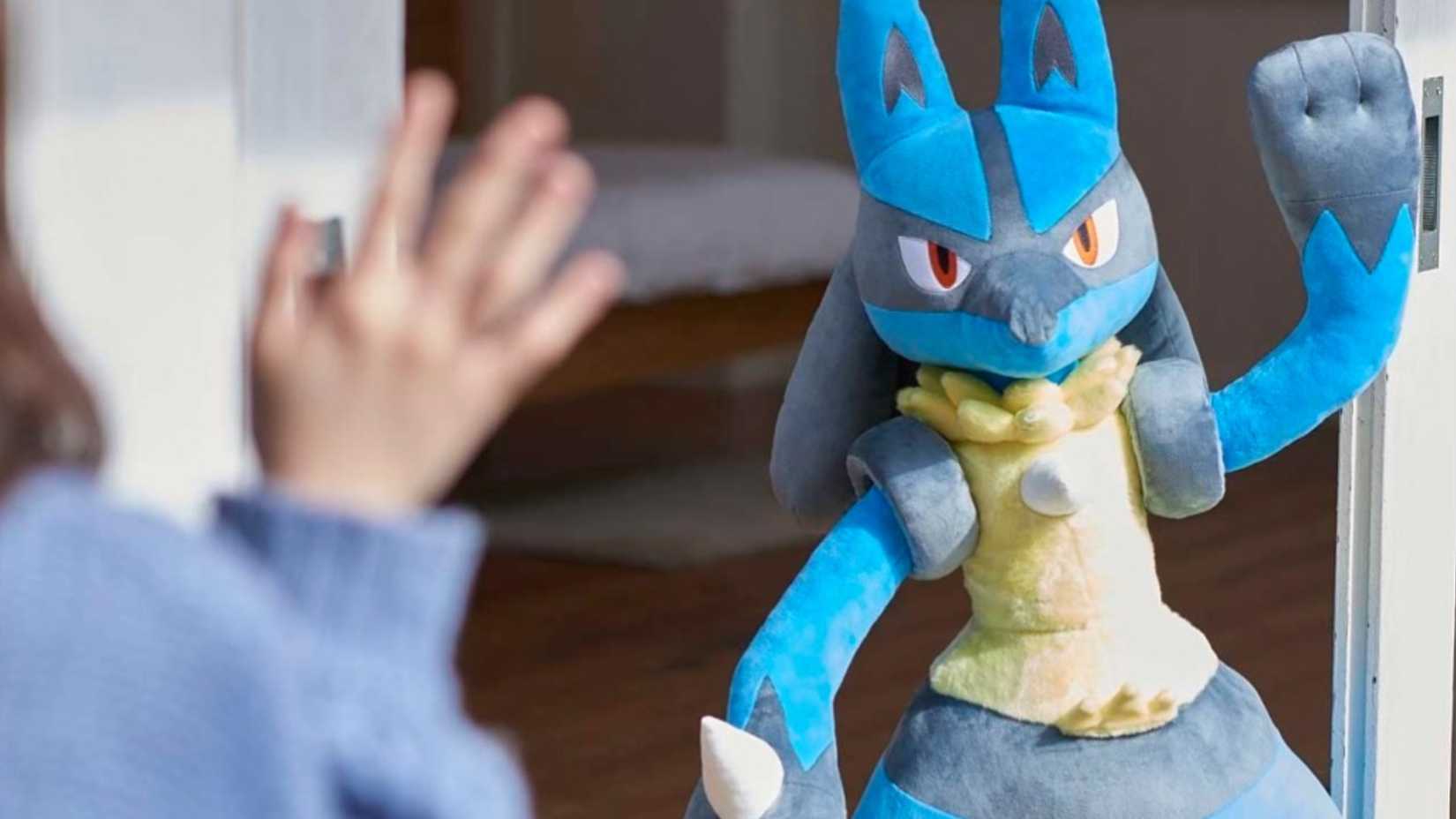 someone waving at a life size lucario plush.