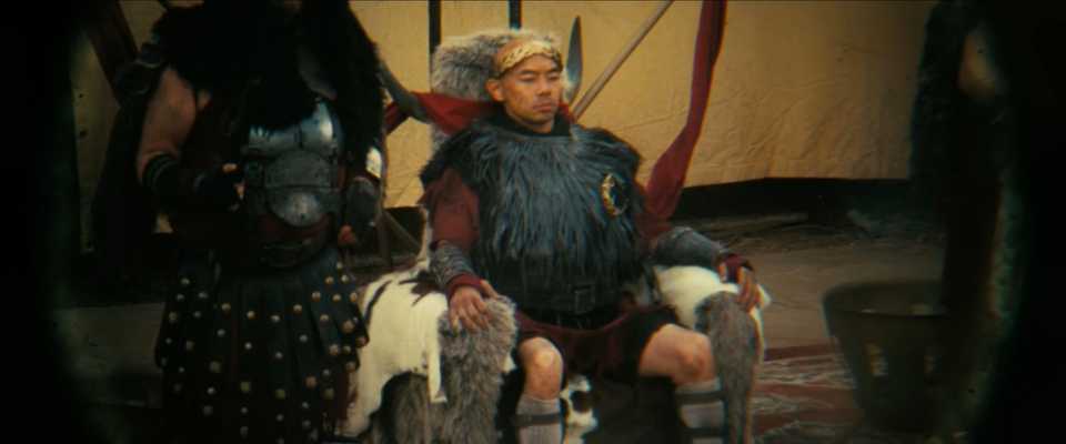 The ghoul is looking through binoculars at one of the two Caesars sitting on his throne.