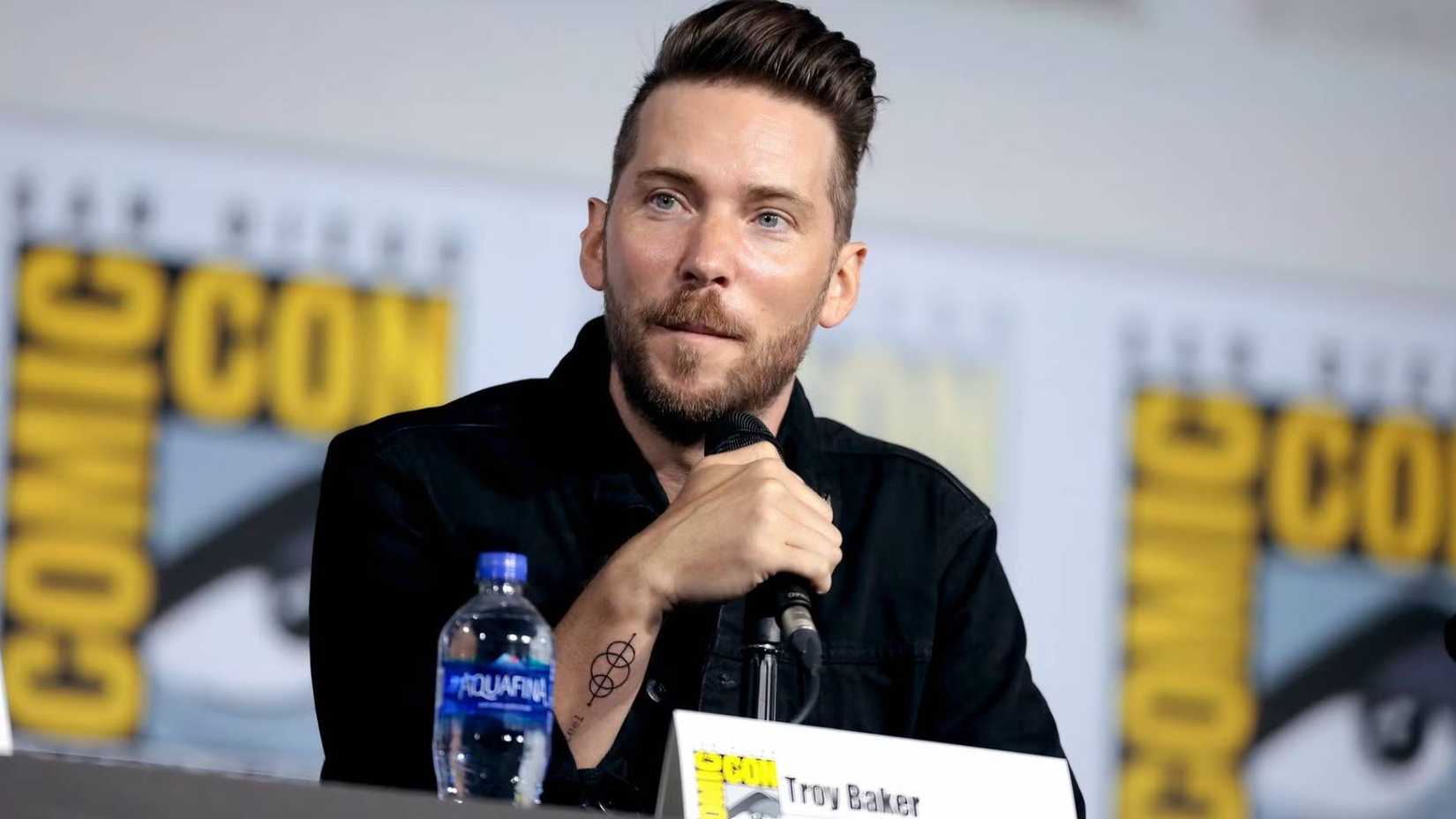 Troy Baker speaks on a microphone at San Diego Comic Con.