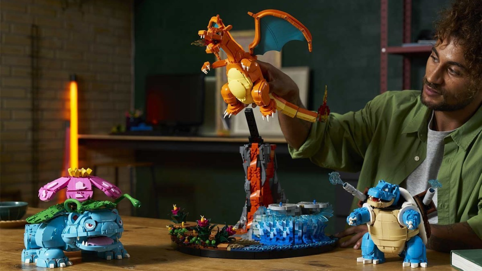 A man playing with Lego Blastoise, Venusaur and Charizard.