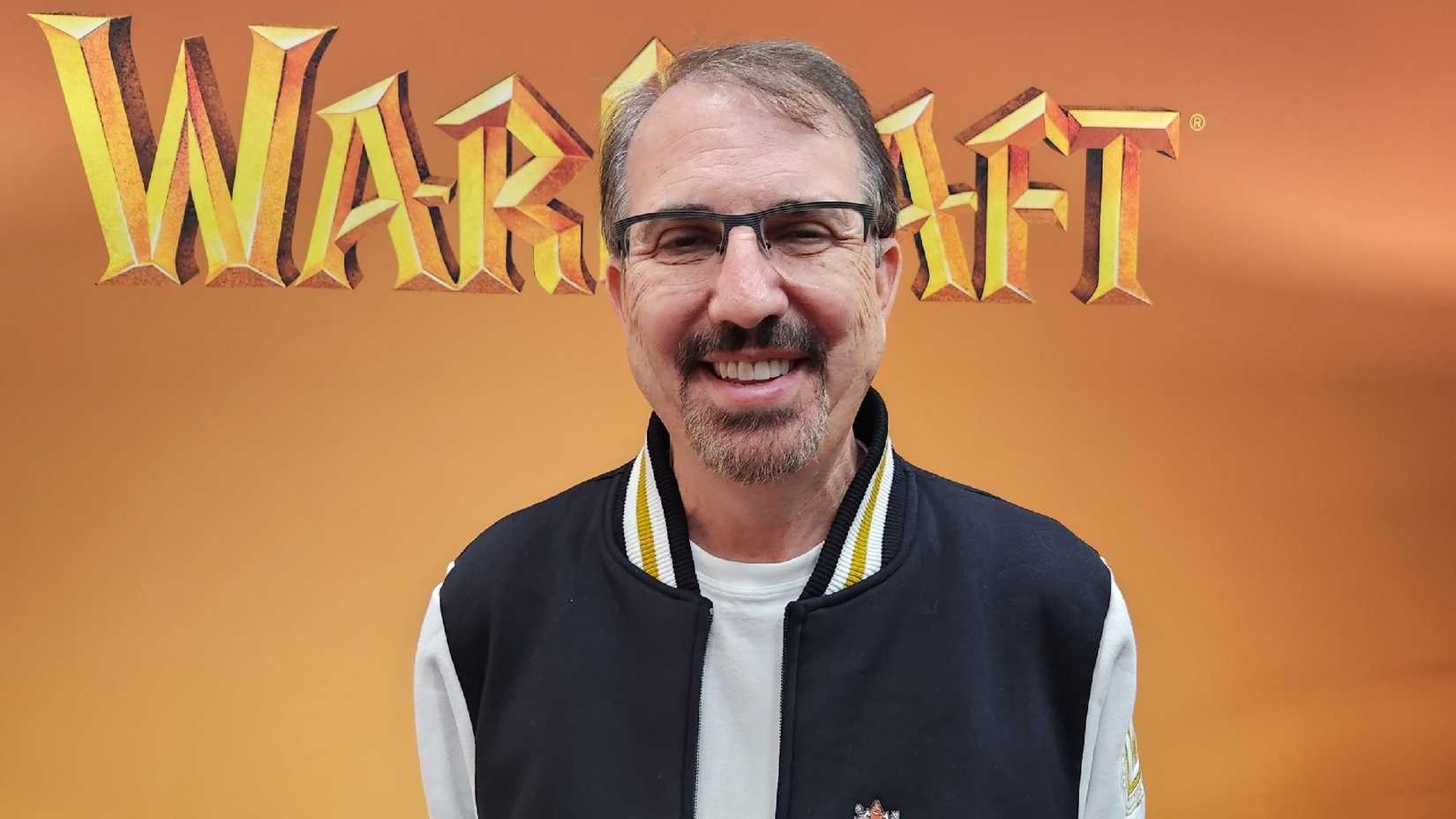 A photo of John Hight stanting in front of a World of Warcraft promotional poster.