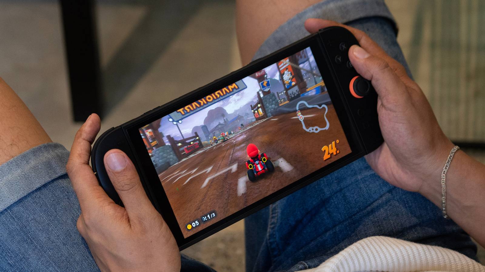 Person in shorts sitting with a Nintendo Switch 2, playing Mario Kart World.