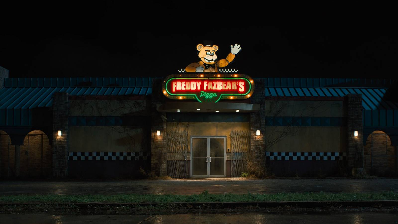 FNAF movie screencap of the Freddy Fazbears pizzeria at night, with the neon sign lit up.
