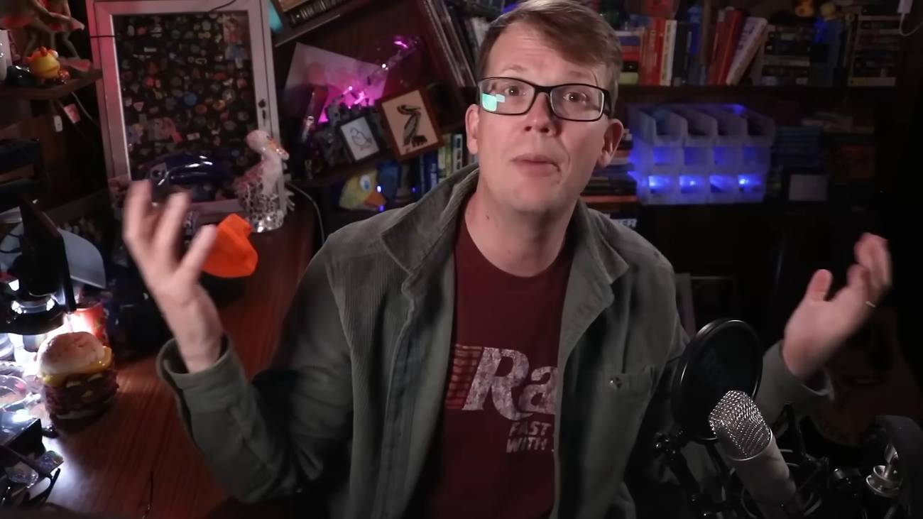 Hank Green with his arms to his side, sitting at his desk for a YouTube video in front of a mic.