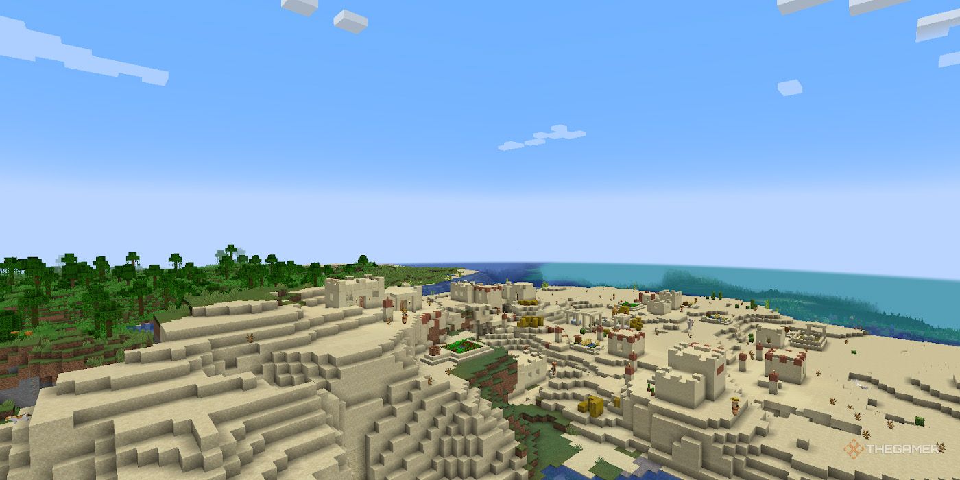 In Minecraft's creative mode, a player observes an aerial view of a desert bordering the ocean.