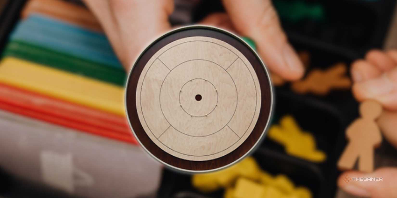 Crokinole board in front of a blurry image of someone preparing to play a board game.