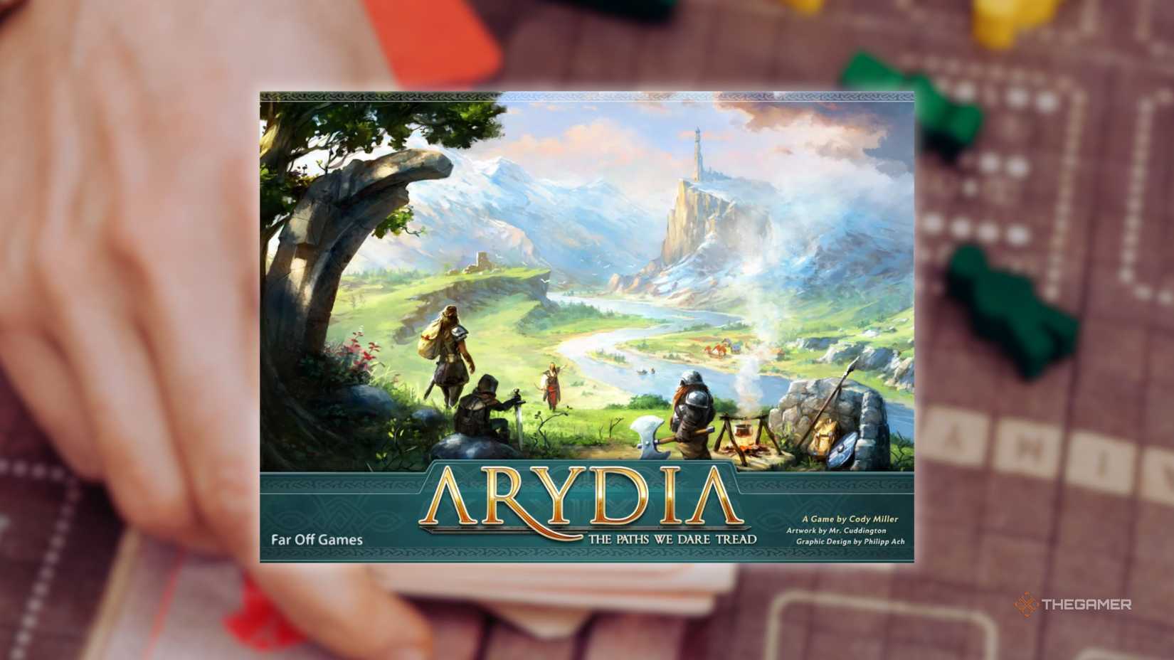 The cover of Arydia in front of a hand playing a grid-based board game for the best board games of 2025.