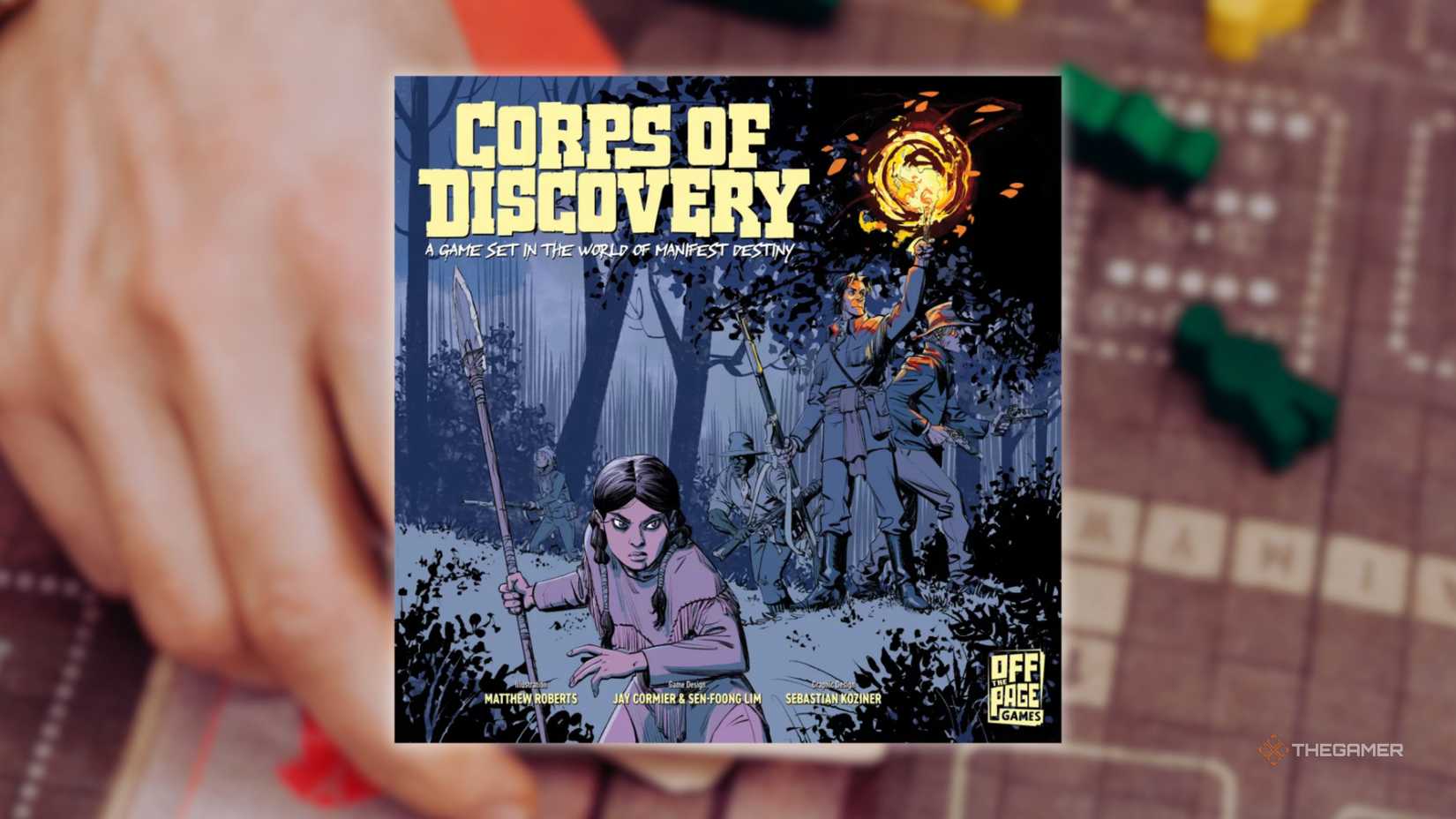 The cover of Corps of Discovery in front of a hand playing a grid-based board game for the best board games of 2025.