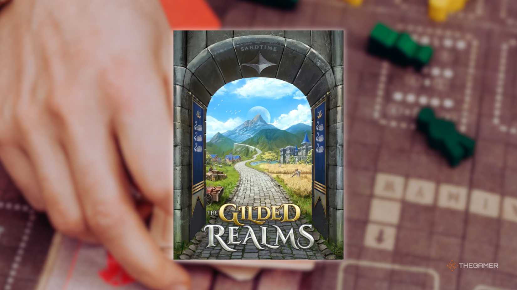 The cover of The Gilded Realms in front of a hand playing a grid-based board game for the best board games of 2025.