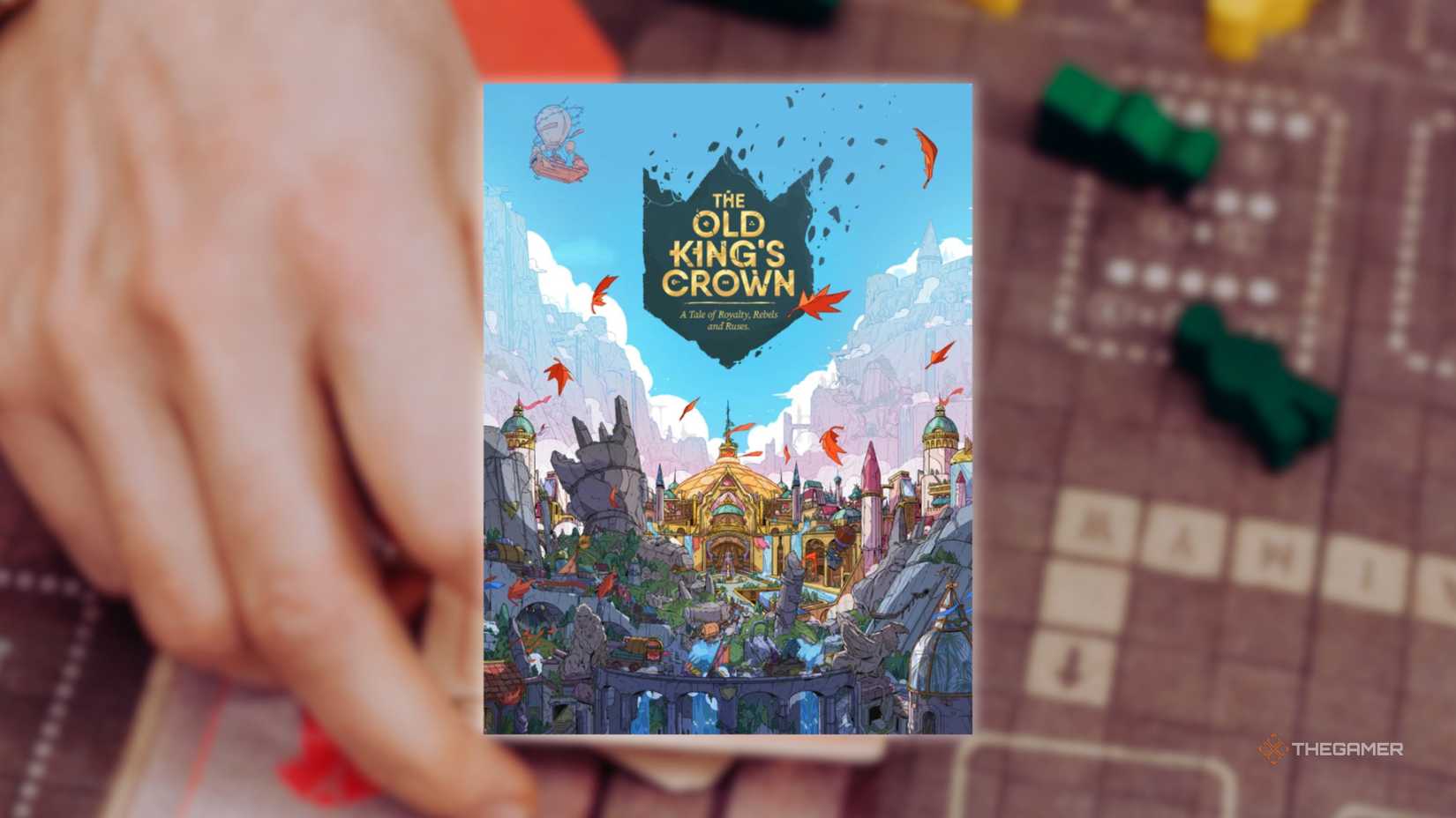 The cover of The Old King's Crown in front of a hand playing a grid-based board game for the best board games of 2025.