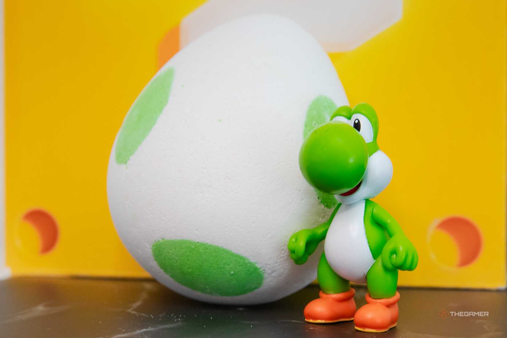 A Yoshi statue next to a giant Yoshi Egg bath bomb from the Lush x Super Mario Galaxy collection.