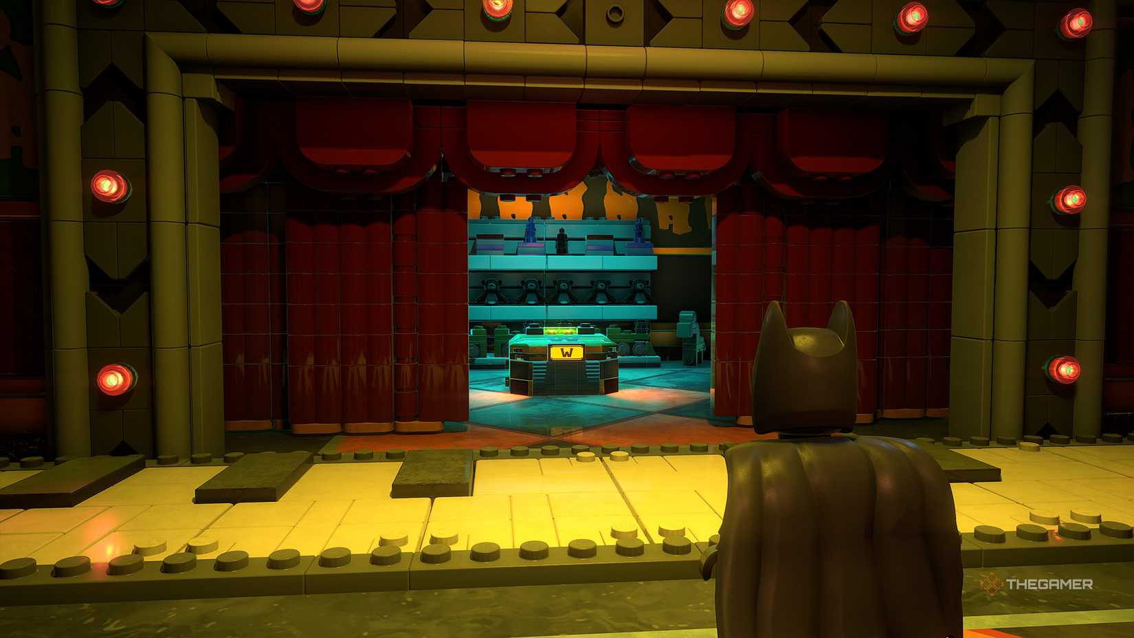 Batman stands in front of a giant piano with a red curtain revealing a WayneTech Cache in Lego Batman Legacy of the Dark Knight.