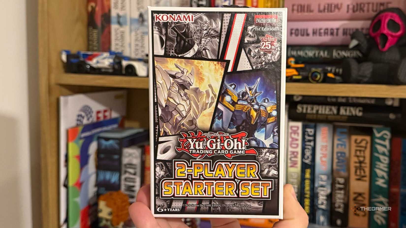 An image of the YuGiOh two player starter deck being held in front of a bookcase.